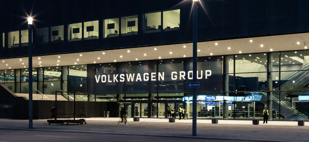 Außenansicht der modernen Volkswagen Group Zentrale bei Nacht, beleuchtet und mit einigen Personen, die vorbeigehen.