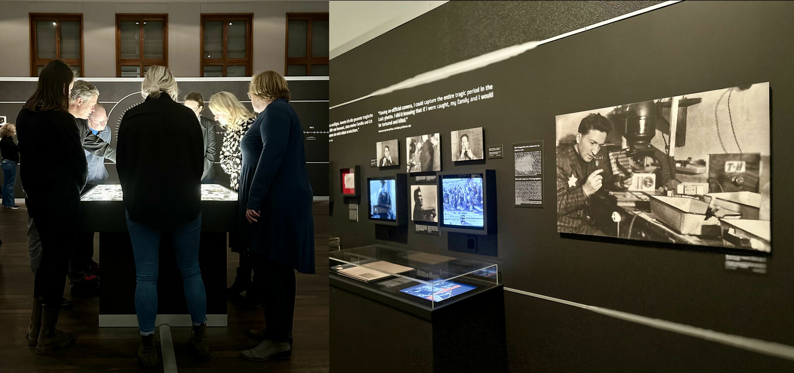 An exhibition featuring historical photographs and documents. On the left, several people in a dimly lit room examine illuminated exhibits in a display case. On the right, a wall showcases various screens with historical film footage and a large photograph of a man at a workbench.