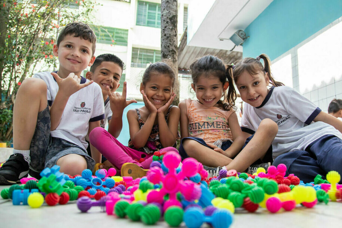 A group of happy children playing with colorful construction toys outdoors.