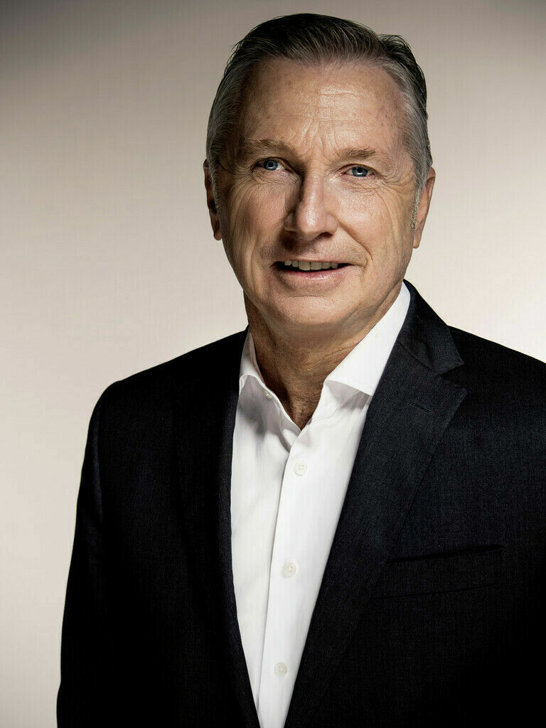 Portrait of a man in a suit and shirt with a friendly expression, set against a neutral background.