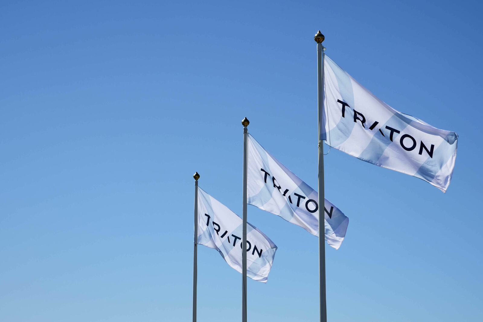 Three waving TRATON flags against a blue sky, symbolizing the company and its global reach.