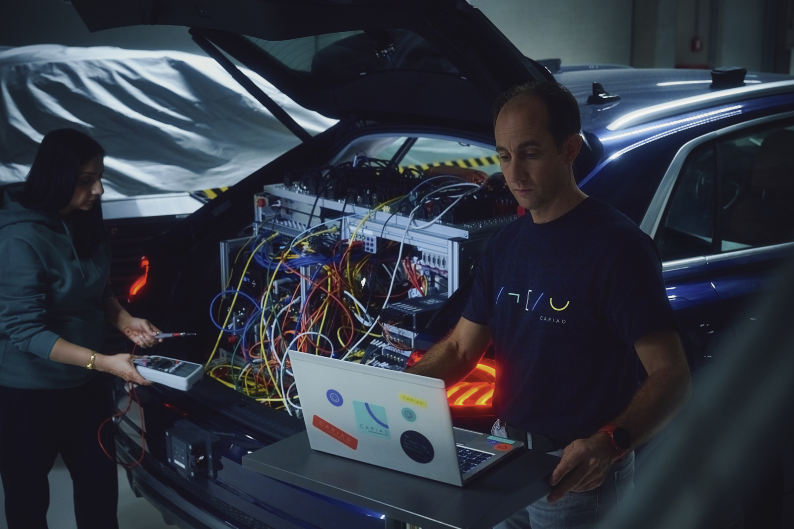 Two people testing a complex technical setup in the trunk of a car.
